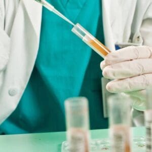 A person in white lab coat holding a syringe.