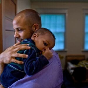 A man holding his son in the arms of another man.