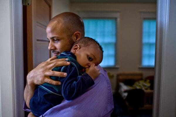 A man holding his son in the arms of another man.