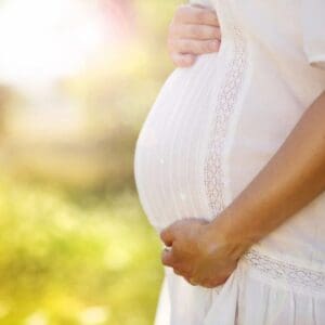 A pregnant woman standing outside in the sun.